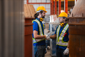 Two man industrial workers wearing safety gear shaking hands inside factory, symbolizing teamwork, trust, and collaboration in professional industrial environment.