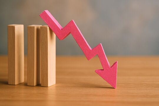 Pink downward zigzag arrow trending downward across wooden blocks on table representing market decline, economic recession and financial crisis concept