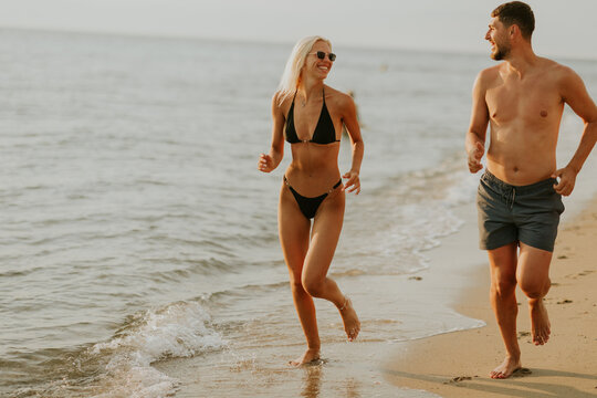 Joyful couple enjoying a beach run during sunset in warm weather - Powered by Adobe