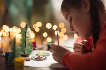 child paints handmade Christmas tree decoration made from salt dough. girl makes crafts for the new year in school
