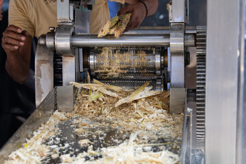 Sugarcane juicing machine on a market stall in India, fresh pressed juice from stalks, squeeze the sweet fruit drink from the cane 