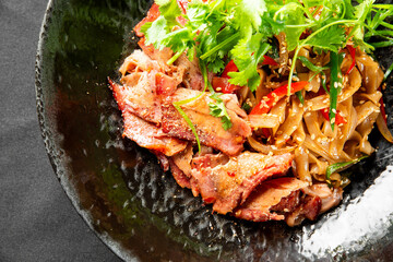 Asian-style pork slices with cilantro, served alongside vegetable noodles with sesame seeds on a...
