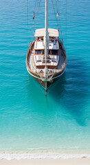 Wooden sailboat in turquoise water near sandy beach, showcasing nautical theme and summer vacation concept