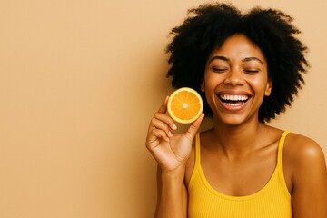 Afro woman in yellow top holding orange slice near head and laughing against beige background, joyful citrus concept