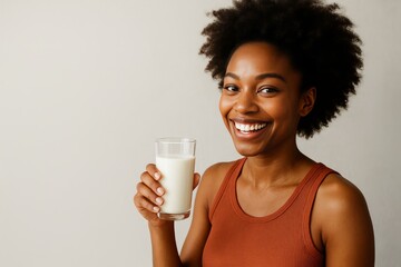 Smiling young woman with afro hair holding a glass of milk against neutral beige background