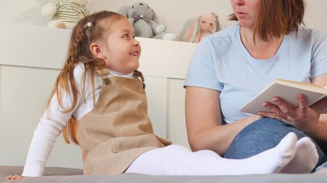 Toddler girl listens as her nanny reads a story aloud. Teaching literacy and imagination in a comfortable setting. Close up.