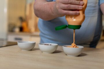 Hand Squeezing Flavorful Condiment into Colorful Bowls for a Delicious Culinary Experience