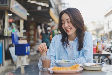 Smiling Asian woman eating Thai breakfast at local street food market, authentic lifestyle and happiness concept.