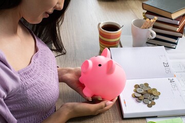 A woman is saving her money with the help of a piggy bank and a cup of coffee in hand