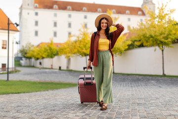 Woman tourist walking with suitcase on the street in European old city, admiring architecture and...