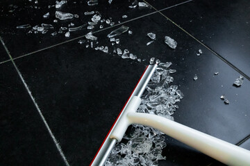 Broom sweeping broken glass shards on black tiled floor for safe clean up