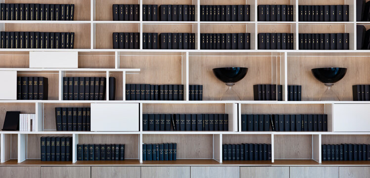 Modern law office library with minimalist design: clean white shelves, monochrome legal books, soft lighting, neutral tones, sleek desk, near large windows create a calm, professional atmosphere.