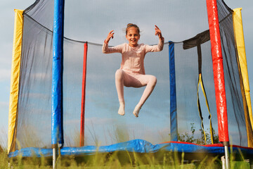 A happy and energetic young girl is captured mid-air while jumping on a trampoline, smiling joyfully at the camera.