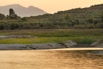 Paisaje anaranjado del atardecer sobre el pantano de Beniarres y silueta al fondo del parque natural sierra de Mariola, España