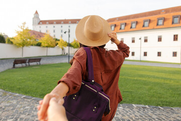 Follow me concept and traveling together. Woman wearing hat and backpack, holding friend's hand and...
