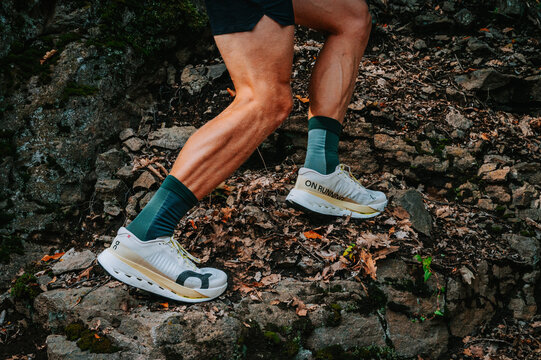 On Cloudultra Pro white trail running shoes with carbon plate on rugged trail, professional runner ascending rocky terrain, close-up on legs in action