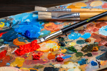Fototapeta premium Old used brushes in an artist's studio, palette with multi-colored spots of oil or acrylic paint