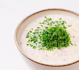 Creamy soup topped with green herbs in a bowl on a light surface