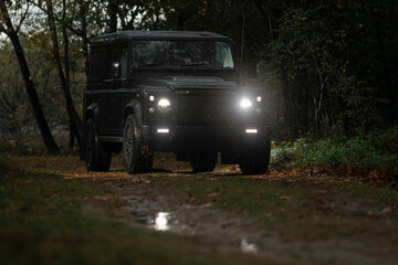 Black 4x4 vehicle parked in dark forest setting with headlights and auxiliary lights on © Victor