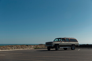Vintage SUV wagon on coastal road with ocean cliffs and clear blue sky
