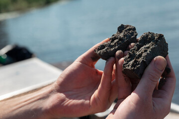 Researcher hands holding soil samples with Dutch windmills and boat visible in pastoral background scene