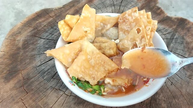 Indonesian meatballs served with noodles, tofu, and fried wontons (pangsit) on a wooden table.street food.