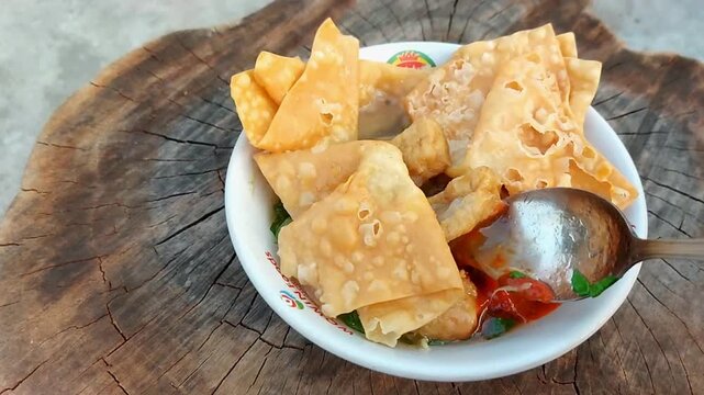 Indonesian meatballs served with noodles, tofu, and fried wontons (pangsit) on a wooden table.street food.