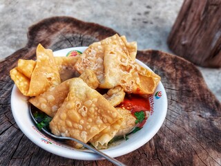 Indonesian meatballs served with noodles, tofu, and fried wontons (pangsit) on a wooden table.street food.