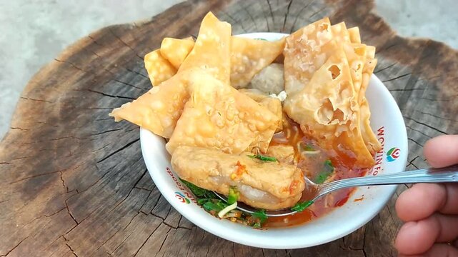 Indonesian meatballs served with noodles, tofu, and fried wontons (pangsit) on a wooden table.street food.