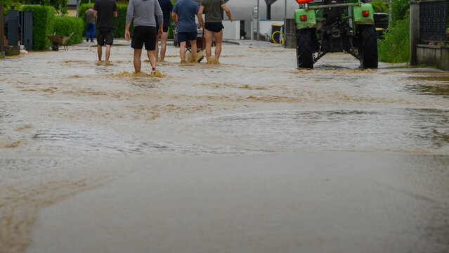 Floodwaters cover streets as residents navigate through knee-deep water, while a tractor assists in cleanup efforts during the flood.
