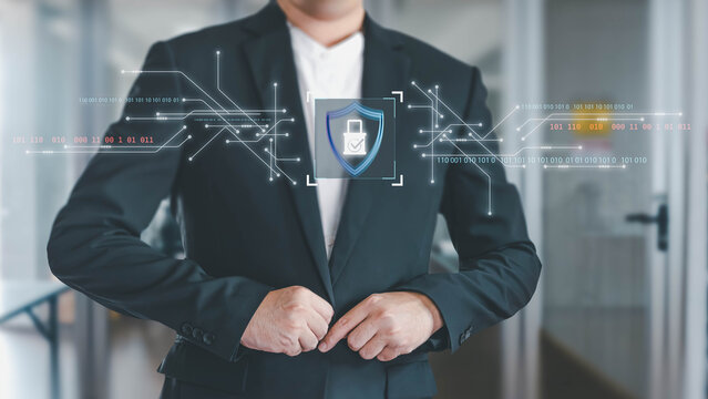 A businessman buttons his suit, standing before a holographic interface displaying a security shield and binary code, symbolizing robust cybersecurity and data protection in a corporate setting.