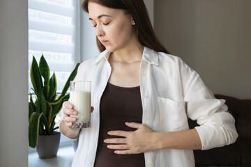 Female with closed eyes holding milk glass feeling abdominal pain. Concept of lactose intolerance,...