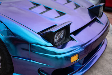 Close-up of the pop-up headlights on a classic sports car with a stunning iridescent blue and purple vinyl wrap, highlighting its JDM style.