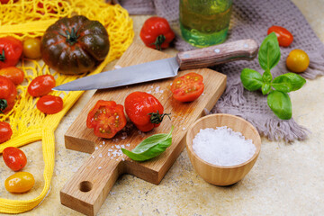 Organic tomato halves on cutting board with basil leaves, coarse salt and eco-friendly kitchen...