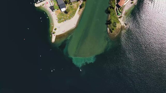 Aerial top down view of river Sarca flowing into Lake Garda with paddle boat, Torbole beach and turquoise water, Italy