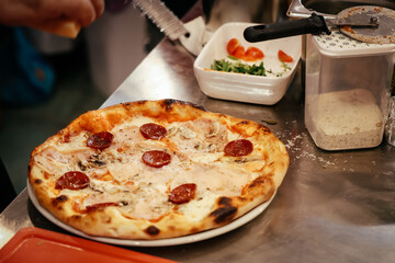 Freshly baked pizza being prepared in a pizzeria kitchen, with ingredients, tools and authentic working environmen