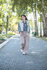 Fototapeta premium Full-length portrait of a young beautiful girl in a checkered shirt and beige pants