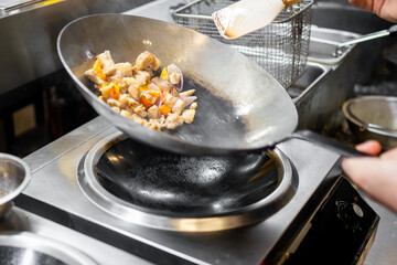 Chef stir-frying meat and vegetables in a wok over a stove, showcasing dynamic cooking motion in a professional kitchen setting.