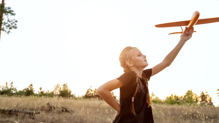Child aviator with airplane dreams of traveling in summer in nature at sunset. Girl with plane on...