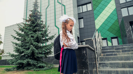 Schoolgirl sadness standing against modern school. Long-haired girl feels bullied by classmates at...