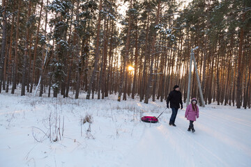 Father and daughter having fun with snow tube in the forest