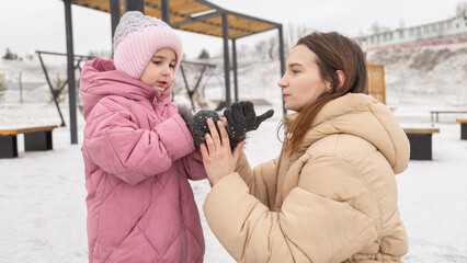 Mother and little girl have fun during winter outdoor. Mom playing with kid on fresh frosty air in...