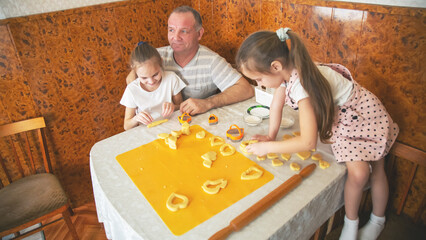 Children cooking cookies together with grandpa in the kitchen