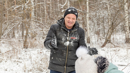 Little girls play with snow with her grandfather in winter forest