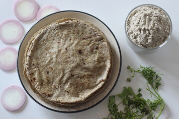 Bajra roti on plate with bajra atta, onion slices, and herbs staple Indian food evoking tradition