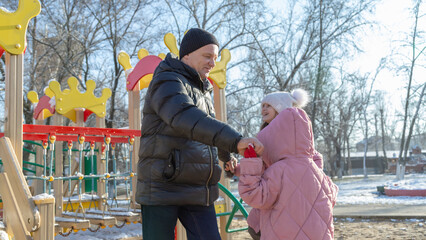 Grandfather with grandchildren playing on the playground on a cold winter day
