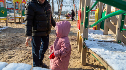 Grandfather playing with his granddaughter on the playground in the park in winter