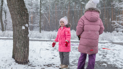 Two little girls in colorful clothes play outdoors during a snowfall.