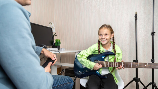 Music teacher and teenage student girl sitting on sofa learning to play on guitar in private lesson in living room at home - Powered by Adobe