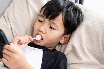 asian boy is lying in his bedroom eating a lollipop while resting, highlighting the risks of...
